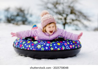 Active Toddler Girl Sliding Down The Hill On Snow Tube. Cute Little Happy Child Having Fun Outdoors In Winter On Sledge . Healthy Excited Kid Tubing Snowy Downhill, Family Winter Time.