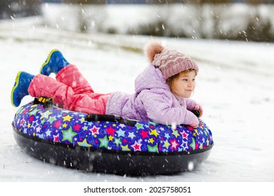 Active Toddler Girl Sliding Down The Hill On Snow Tube. Cute Little Happy Child Having Fun Outdoors In Winter On Sledge . Healthy Excited Kid Tubing Snowy Downhill, Family Winter Time.