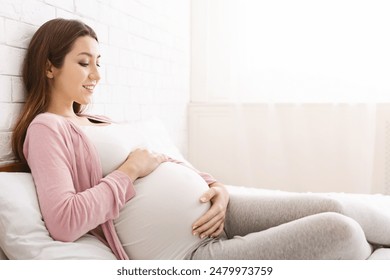 Active unborn baby pushing his mom, pregnant lady enjoying her pregnancy, lying in bed at home, copy space - Powered by Shutterstock