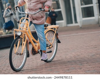 Active urban scene with a cyclist in a pink jacket pedaling a yellow bike on a cobblestone street