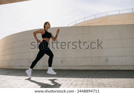Active woman athlete is jogging in morning on modern building background. Healthy life concept