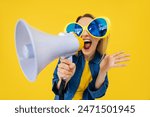 Active woman in comic glasses holding loudspeaker and making advertisement while laughing. Energetic young woman entertaining people while telling funny jokes in megaphone over yellow background.