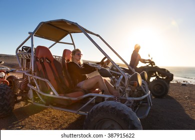 Active woman driving quadbike on dirt road by the sea in sunset.