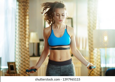 Active Woman In Fitness Clothes Exercise Using A Jump Rope With Heart Rate Monitor At Modern Home.