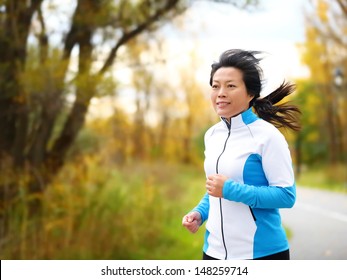 Active Woman In Her 50s Running And Jogging. Middle Aged Asian Mature Female Jogger Outdoor Living Healthy Lifestyle In Beautiful Autumn City Park In Colorful Fall Foliage. Asian Chinese Adult Fifties
