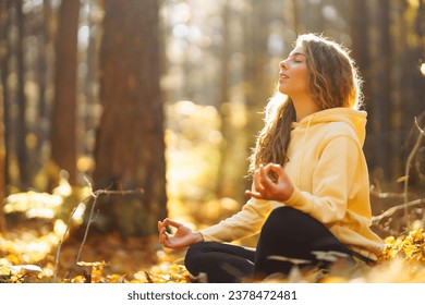 Active woman practices yoga in the autumn forest among yellow fallen leaves, catches zen. Concept of meditation, relaxation. Active lifestyle. - Powered by Shutterstock