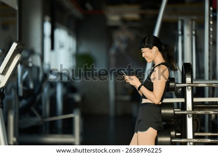 Active woman smiling while checking her phone in a gym during a workout.