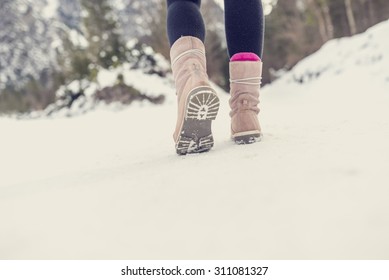 Active woman walking away from the camera through winter snow wearing pale pink boots in the countryside, with copyspace in the foreground. Retro filter effect.