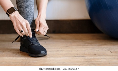 Active woman wearing a smartwatch tying her shoelaces. Fitness gear smart watch, healthy active woman tying her shoelaces. Active person in active apparel, smartwatch and tying shoelaces. - Powered by Shutterstock