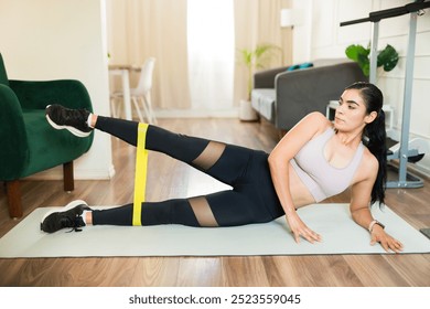 Active woman wearing sportswear using a resistance band while working out on a mat in the living room of her apartment - Powered by Shutterstock