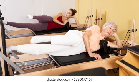 Active women practicing Pilates in a fitness studio perform a stretching exercise on a reformer bed - Powered by Shutterstock