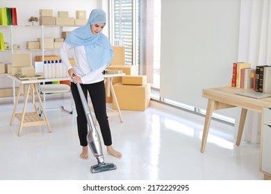 Active Young Beautiful Asian Housewife Woman Cleaning With Vacuum Cleaning Floor After Working SME With E-commerce Package Box Background. Cleaning Girl In Muslim Black Leggings Vacuuming Her Room.