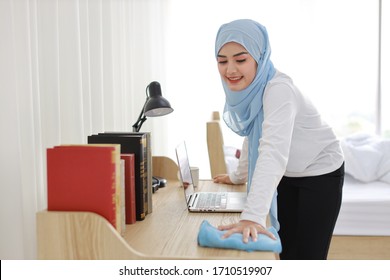 Active Young Beautiful Asian Muslim Housewife Woman In Sleepwear Cleaning Up Wooden Table With Computer. Portrait Cute Girl With Happy Emotional Cleaning Bedroom In New Apartment After Moved In. 