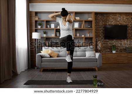 Active young brunette in sport clothes standing on yoga mat and making criss cross crunches exercise. Multiracial healthy woman training abs during domestic workout.