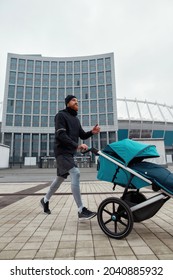 Active Young Dad In Sportswear Training And Pushing Stroller With A Child In The City On A Cold Autumn Day. Parenting, Healthy Lifestyle, Sports Concept