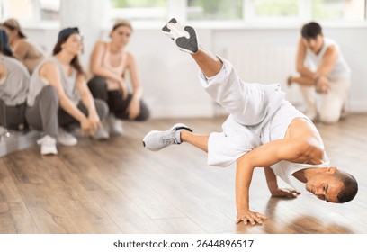 Active young guy breakdancing in front of other attendees of dancing classes in training hall