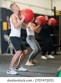 Active young guy working out with medicine ball in gym during weight training classes