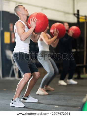 Active young guy working out with medicine ball in gym during weight training classes