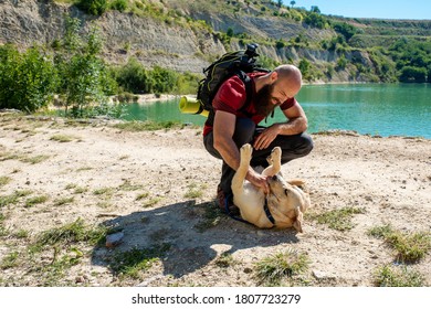 Active young hiker playing with his dog on hike in high mountains with beautiful lake in the background
