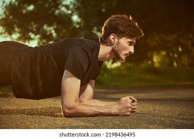 An active young man is doing push-ups from the floor on the ground in the park. Sport and fitness. Active lifestyle.