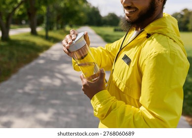 Active young man smiles while holding a water bottle during his spring workout outdoors