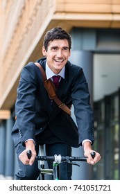 Active young man smiling while riding utility bicycle to his workplace in the morning in a modern European city