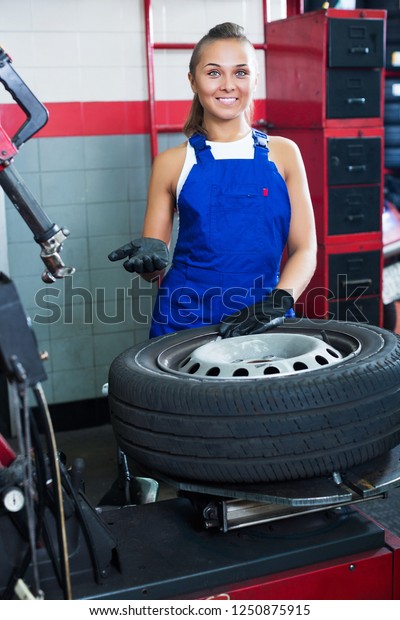 Active young mechanic woman working on car wheel in\
service point