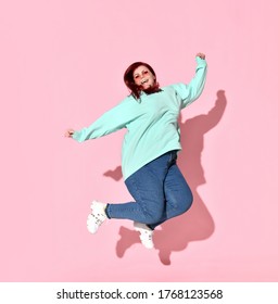 An active young overweight female in casual clothes and glasses jumps, full of happiness and joy. Self-esteem, active lifestyle, charming plus-size, positive body. Studio shot isolated on pink.