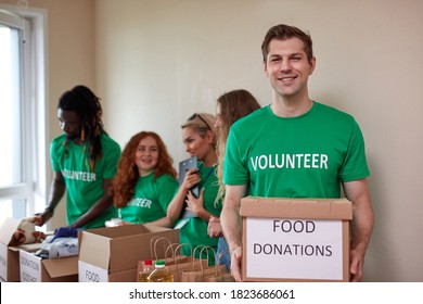 Active Young People Enjoys Volunteering At Food And Clothes Bank, Voluntary Company. Diverse People Working In Voluntary Company With Friends Putting Food For Donation Into Boxes