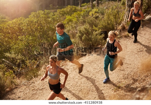 Active young people running on mountain trail.\
Top view of running club members training together through trails\
on the hillside\
outdoors.