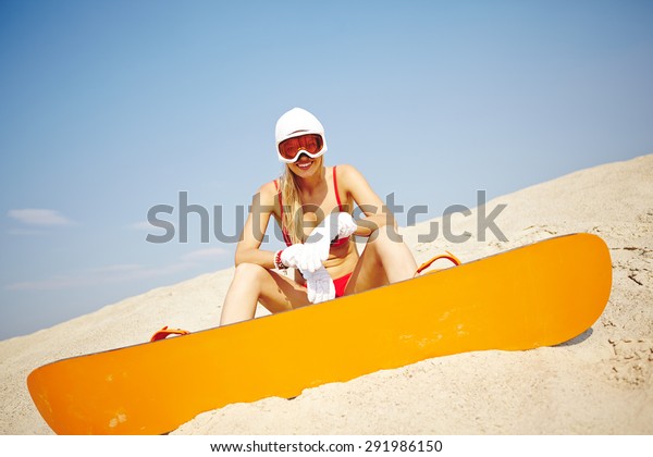 Active\
young sandboarder in red bikini sitting on\
sand