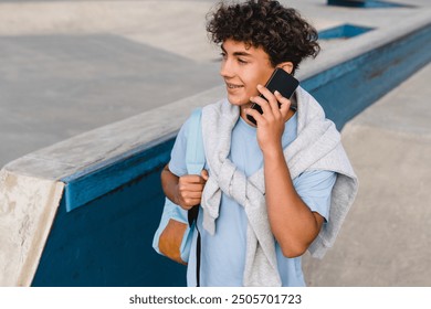 Active young teen boy skater in smart casual clothes with braces holding bag standing against ramp in city skate park urban street talking on mobile cell phone spending time after school lessons - Powered by Shutterstock