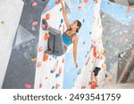 Active young woman engaged in bouldering activity in rock climbing hangar