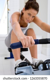 Active Young Woman Exercising At Home On Rowing Machine At Camera