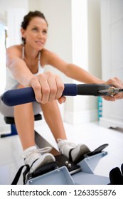 Active Young Woman Exercising At Home On Rowing Machine