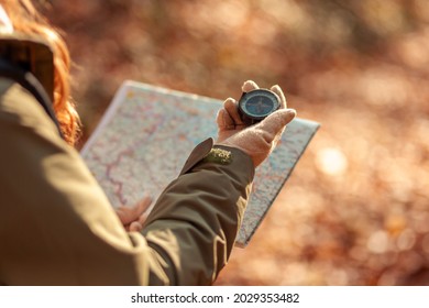 Aktive junge Frau, die einen Kompass hält und eine Karte liest, während sie eine Wanderpause macht, Spaß hat und sich während des Herbsttages im Freien entspannt