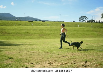 Active young woman jogging with her dog across open grassy field on a sunny day. Healthy lifestyle and wellness concept - Powered by Shutterstock