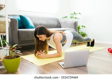 Active young woman watching an online workout video on her laptop and doing a forearm plank pose. Fit latin woman exercising at home - Powered by Shutterstock