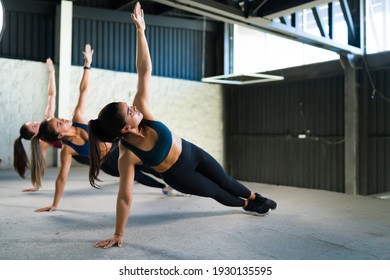 Active Young Women Doing A Side Plank And Looking Up. Athletic Women Showing Their Strength During A HIIT Class At The Gym