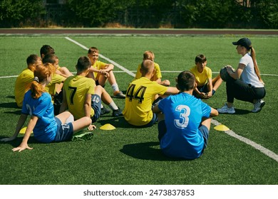 Active Youth Engagement. Children sitting on grass and listening to female football coach instructions, learning soccer game strategies and skills. Sport, school, childhood, active lifestyle concept - Powered by Shutterstock