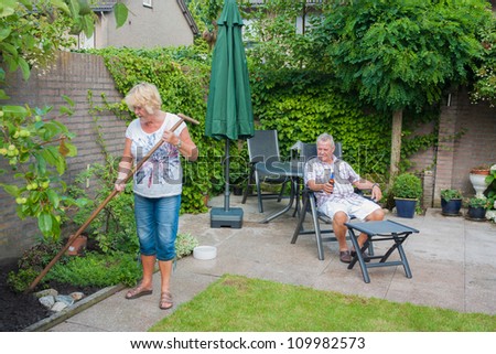 Actively retired Dutch seniors in a Typical display of gender roles where the Wife is gardening and the husband is relaxing and having a beer