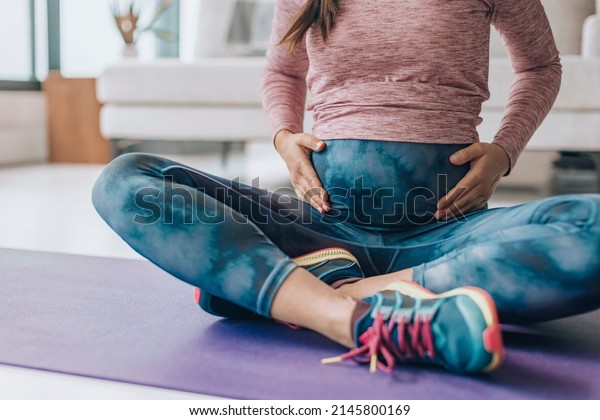 Activewear for pregnancy. Maternity clothes woman\
wearing full panel yoga leggings for bodyweight workout at home on\
floor mat