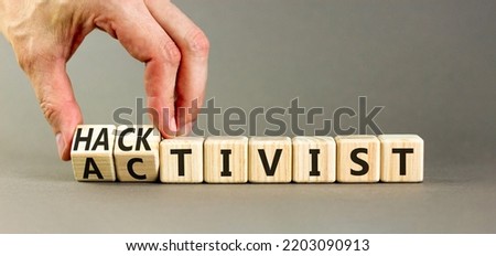 Activist or hacktivist symbol. Businessman turns wooden cubes and changes the word Activist to Hacktivist. Beautiful grey table grey background, copy space. Business activist or hacktivist concept.