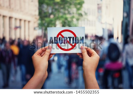 Activist hands holding a banner with stop abortion message over a crowded street background. Social awareness concept, humanity problems say no to abortion. Fetus rights law and reproductive justice. Stock photo © 