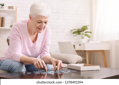 Activity can improve brain function. Elderly woman sitting at table and sorting jigsaw puzzle pieces, free space