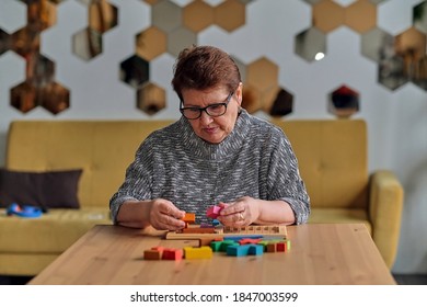 Activity Can Improve Brain Function. Elderly Woman Sitting At Table And Sorting Jigsaw Puzzle Pieces, Free Space Game