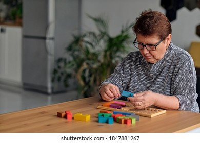 Activity Can Improve Brain Function. Elderly Woman Sitting At Table And Sorting Jigsaw Puzzle Pieces, Free Space Game