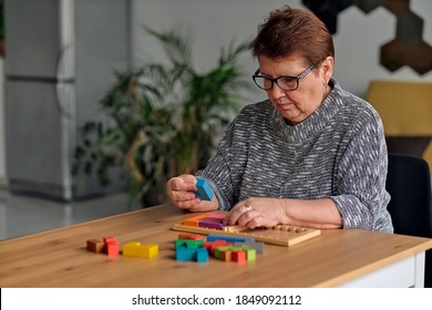 Activity Can Improve Brain Function. Elderly Woman Sitting At Table And Sorting Jigsaw Puzzle Pieces, Free Space Game