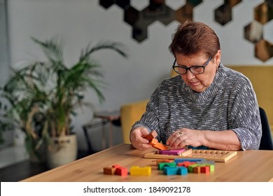 Activity Can Improve Brain Function. Elderly Woman Sitting At Table And Sorting Jigsaw Puzzle Pieces, Free Space Game