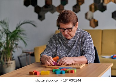 Activity Can Improve Brain Function. Elderly Woman Sitting At Table And Sorting Jigsaw Puzzle Pieces, Free Space Game